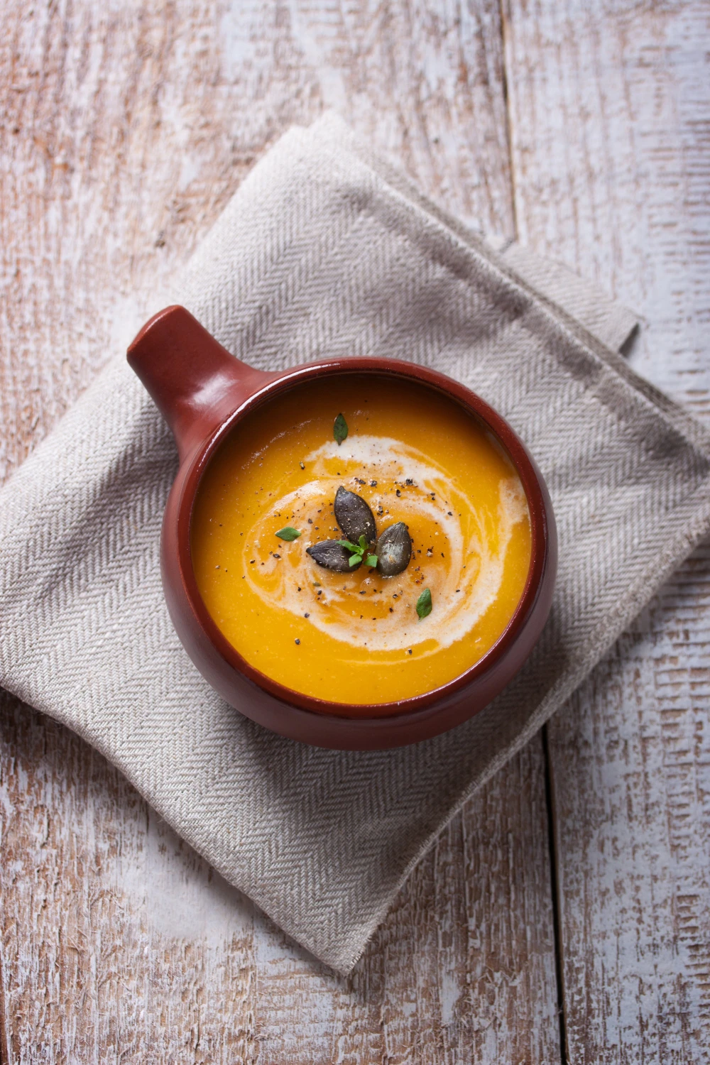 Horizontal Image (Featured Image) — 16:9 aspect ratio: Horizontal food photography of a pot of butternut squash soup with a ladle resting inside, roasted squash cubes and fresh sage scattered nearby, warm kitchen setting with soft natural light, linen napkin softly blurred in the background, high resolution, appetizing and inviting food styling.